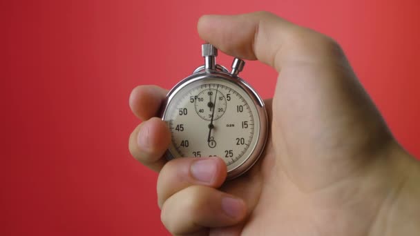 Male hand holding analogue stopwatch on red background. Time start with old chronometer man presses start button in the sport concept. Time management concept. - Footage, Video