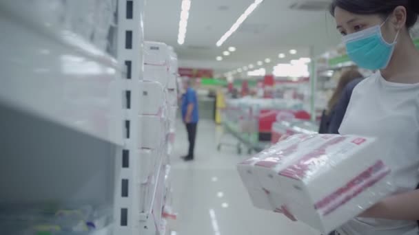 Młoda azjatycka maska damska wybierająca papier ręcznikowy w sklepie spożywczym podczas kryzysu COVID-19, zaopatrzenie w zapasy, profilaktyka rozprzestrzeniania się wirusa korony, nowe normalne życie - Materiał filmowy, wideo