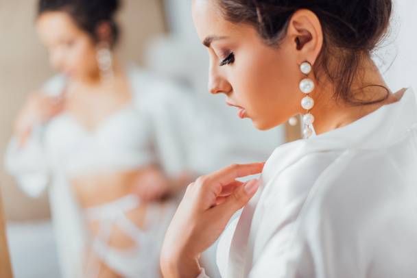 Concentration sélective de la mariée en perle boucle d'oreille touchant robe de soie à la maison - Photo, image