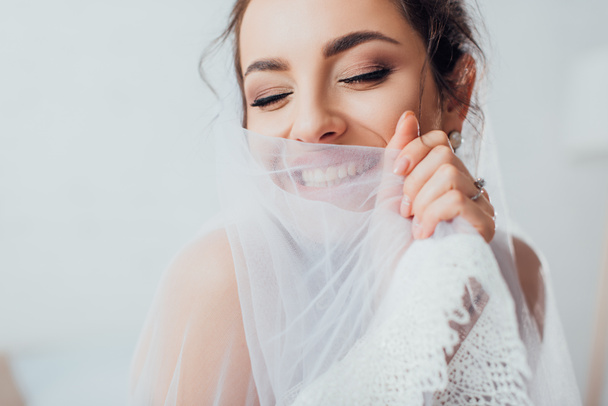 Foco seletivo de noiva morena com olhos fechados segurando véu de renda
  - Foto, Imagem