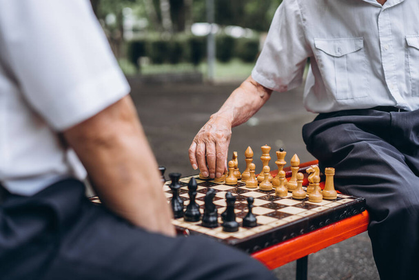 Two senior adult men playing chess on the bench outdoors in the park - Fotoğraf, Görsel
