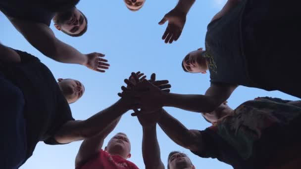 Jovens atletas juntando as mãos, um a um, em unidade. Grupo de melhores amigos colocando seus braços no centro de um círculo e levantando-os para o céu azul. Conceito de amizade e trabalho em equipe
 - Filmagem, Vídeo
