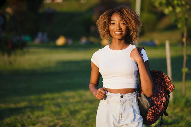 Close up beauty outdoor portrait of attractive charming young african-american smiling woman with natural make up and afro hair, enjoying a day at the park. Outdoor portrait of African girl - Foto, Imagem
