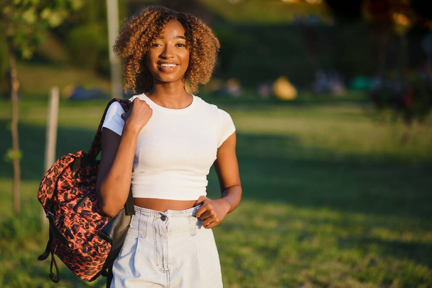 Close up beauty outdoor portrait of attractive charming young african-american smiling woman with natural make up and afro hair, enjoying a day at the park. Outdoor portrait of African girl - Foto, Imagen