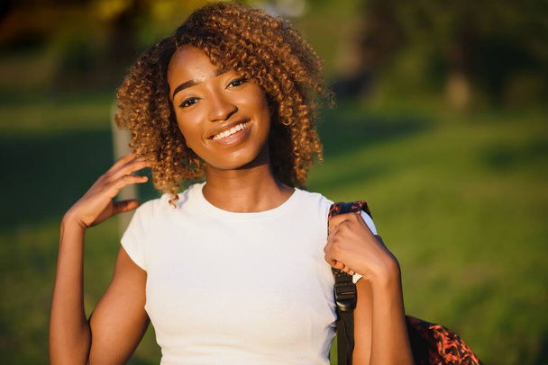 Close up beauty outdoor portrait of attractive charming young african-american smiling woman with natural make up and afro hair, enjoying a day at the park. Outdoor portrait of African girl - Foto, Imagen
