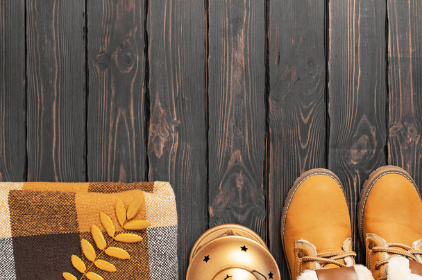 Autumn Fashion Concept. Brown Orange leather women boots with fur, checkered warm plaid, golden autumn leaf on brown wooden background top view. Fashionable womens footwear. Cozy fall composition - Photo, Image