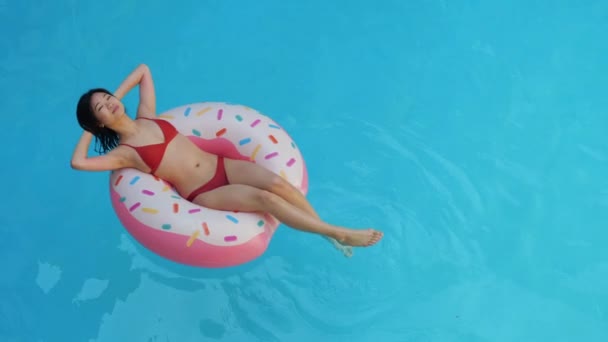 Aziatisch ontspannen meisje in rode lingerie badpak gekoeld door warmte, zwemt op blauw water in spa complex op opblaasbare ring, waardoor golven, dromen, haar handen gevouwen achter haar hoofd, zomervakantie concept - Video