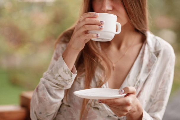 Young female standing after taking a shower in the morning on balcony of the hotel. holding a cup of coffee or tea in her hands. Looking outside nature forest and Mountain - Foto, afbeelding