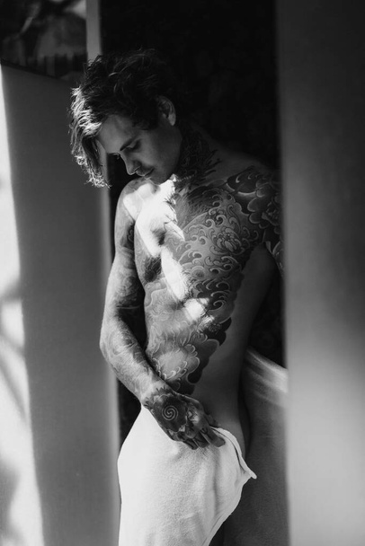 handsome young man in tattoos in the bathroom after a shower in  - Fotó, kép