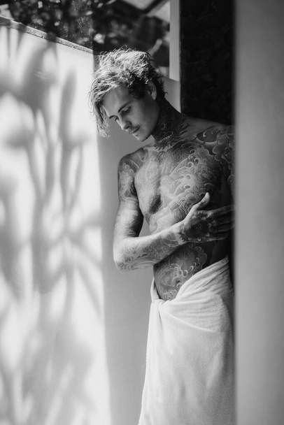 handsome young man in tattoos in the bathroom after a shower in  - Zdjęcie, obraz