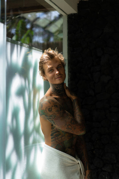 handsome young man in tattoos in the bathroom after a shower in  - Foto, Bild