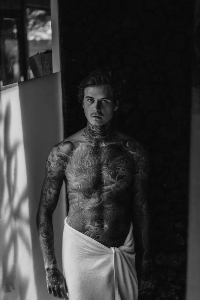 handsome young man in tattoos in the bathroom after a shower in  - Valokuva, kuva