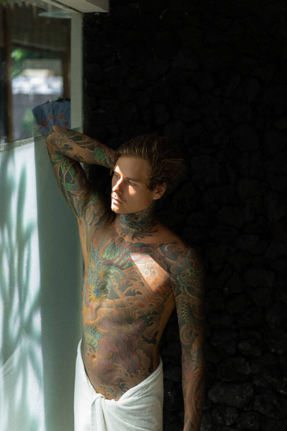 handsome young man in tattoos in the bathroom after a shower in  - Фото, зображення