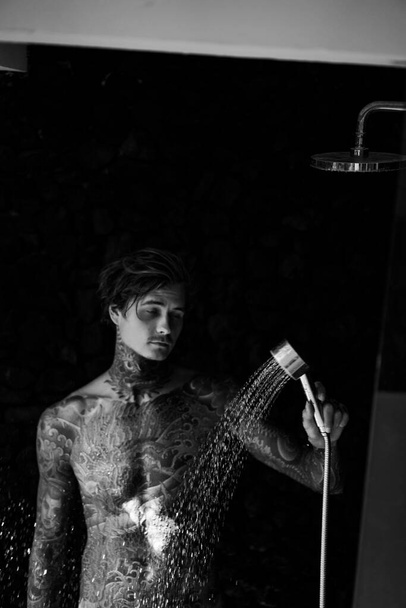 handsome young man in tattoos in the shower. lifestyle concept.  - 写真・画像