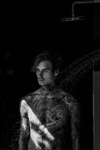 handsome young man in tattoos in the shower. lifestyle concept.  - Photo, Image