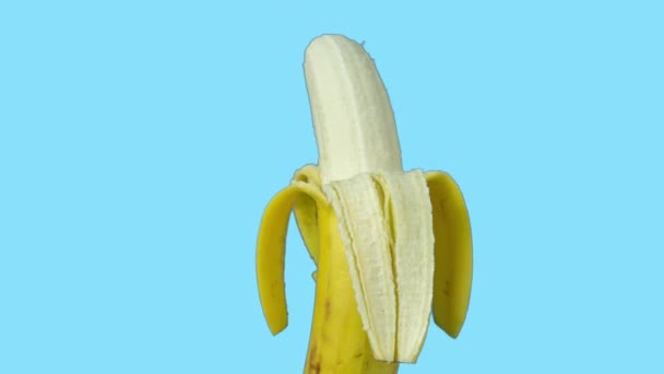 Animierte Aufnahmen einer halb geschälten Banane, die sich vor blauem Hintergrund dreht - Filmmaterial, Video