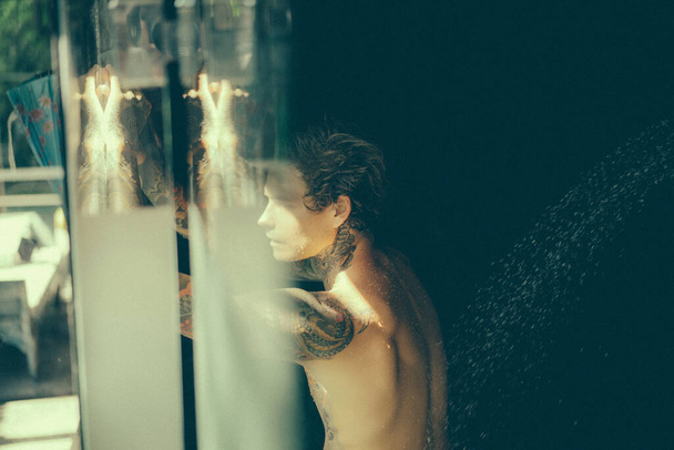 handsome young man in tattoos in the shower. lifestyle concept.  - Fotoğraf, Görsel