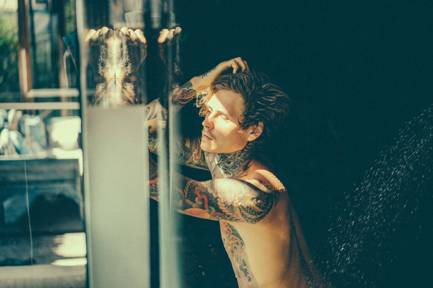 handsome young man in tattoos in the shower. lifestyle concept.  - Fotografie, Obrázek