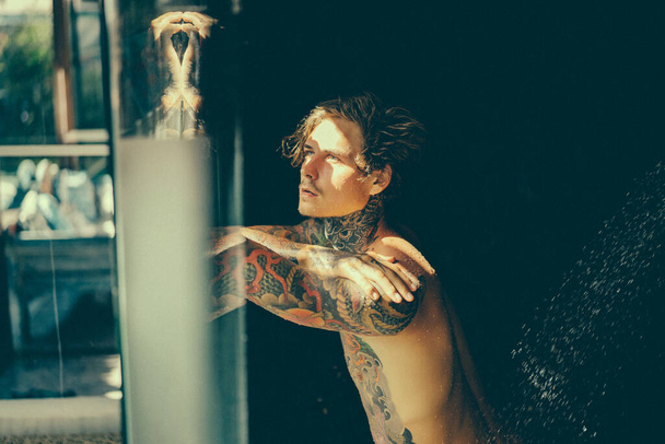 handsome young man in tattoos in the shower. lifestyle concept.  - Foto, immagini
