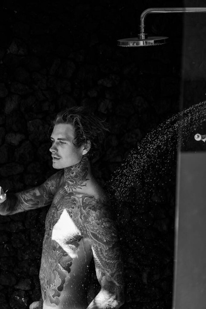 handsome young man in tattoos in the shower. lifestyle concept.  - Foto, afbeelding