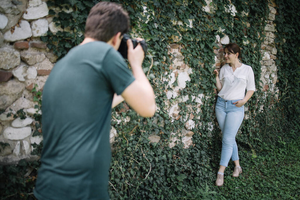 Blurred photographer taking photo session of girl in front of wall with ivy - Valokuva, kuva
