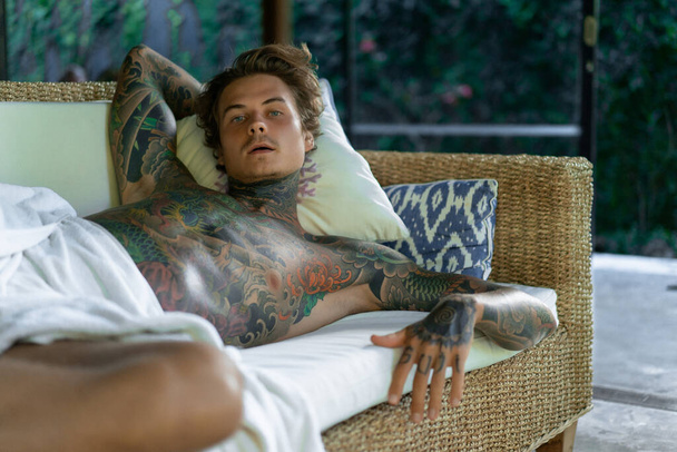handsome young man in tattoos is resting in the living room - Фото, изображение