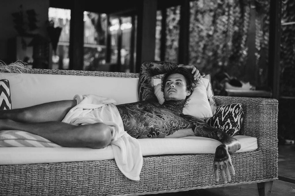 handsome young man in tattoos is resting in the living room - 写真・画像