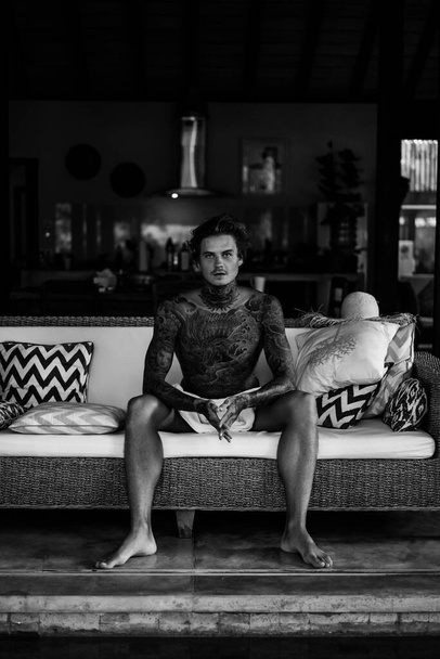 handsome young man in tattoos is resting in the living room - Foto, imagen