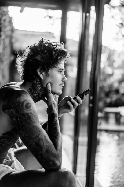handsome young man in tattoos talking on the phone on speakerpho - Фото, изображение