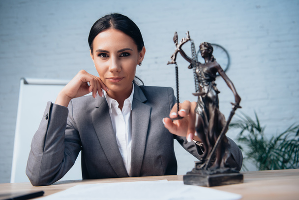 selective focus of lawyer in formal wear touching statuette of justice in office - Foto, Imagen