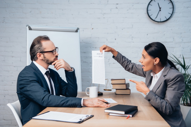 предпринимательница, указывая пальцем на страховой документ рядом с коллегой в очках и разговаривая в офисе - Фото, изображение