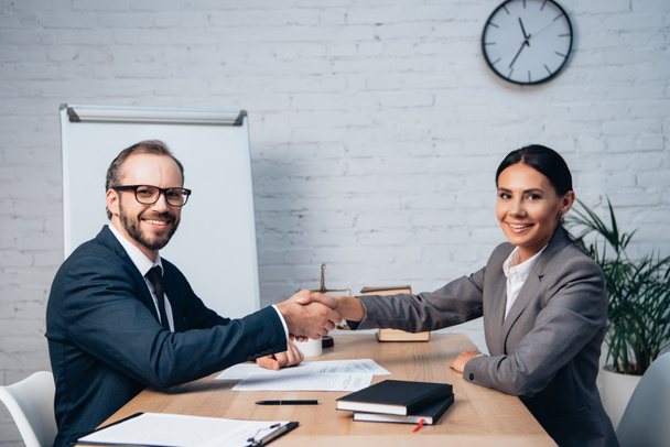 businessman in glasses and businesswoman shaking hands near documents  - Foto, Imagen