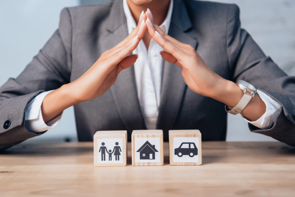 cropped view of lawyer holding hands above wooden cubes with family, car and house  - Foto, imagen