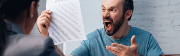panoramic shot of angry and bearded man screaming while holding insurance policy agreement near lawyer  - Photo, Image