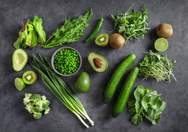 Top view of healthy organic food: cucumbers, scallions, green peas, broccoli, avocado, kiwi fruits, lime and herbson dark background. Source of protein for vegetarians. - Foto, Imagem