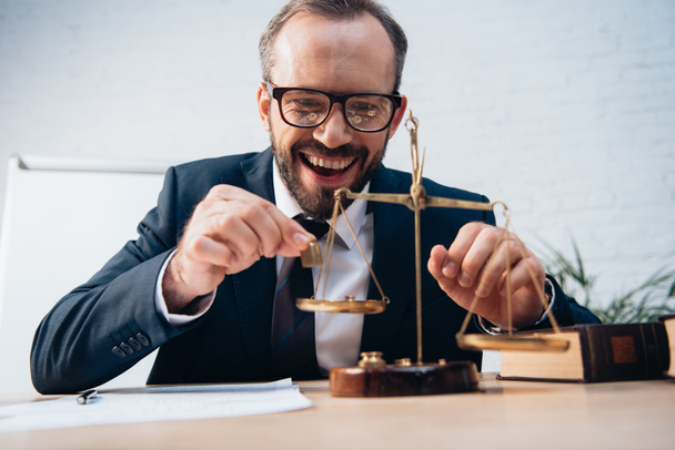 selective focus of excited lawyer holding miniature weights near golden scales - Foto, Imagen