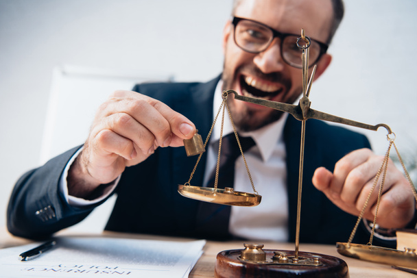 selective focus of excited lawyer in glasses holding miniature weights near golden scales - Photo, Image