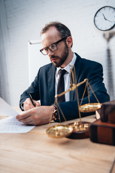 selective focus of bearded lawyer signing insurance documents near golden scales and books - 写真・画像