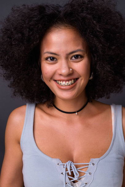 Studio shot of young multi ethnic African American woman with Afro hair against gray background - Photo, Image