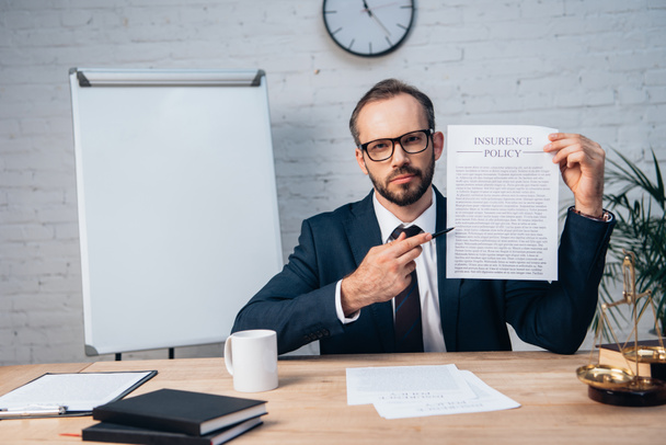 selective focus of bearded lawyer in glasses holding pen and contract with insurance policy lettering in office - 写真・画像