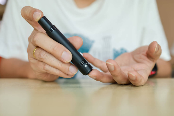 血糖値計で血糖値を確認するために、指にランセットを使用して人の手を閉じてください。医療、糖尿病、血糖値、医療、人々の概念としての使用. - 写真・画像