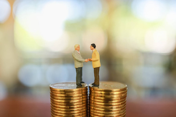 Business Money and Finance Concept, Twee zakenman miniatuur figuur mensen staan en maak een hand schudden op de top van de stapel van gouden munt. - Foto, afbeelding