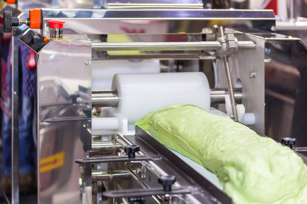 крупным планом тестовый материал для китайских или азиатских продуктов питания фаршированные булочки на конвейере автоматической пищевой машины в производственной линии для высокотехнологичного промышленного производства - Фото, изображение
