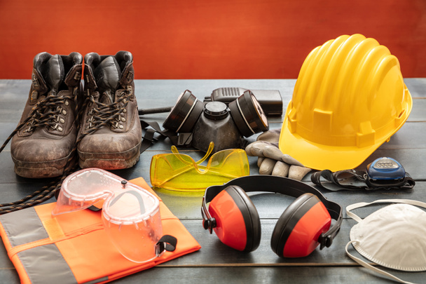 Work safety protection equipment. Industrial protective gear on wooden table, red color background. Construction site health and safety concept - Photo, Image