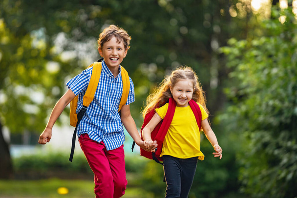Primary school pupil. boy and girl with backpacks walking down the street. Happy children happy to go back to school. beginning school year. Children are happy to run to school. School education. - Photo, image