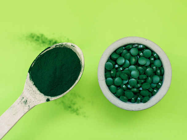 Green hawaiian spirulina in tablespoons pills and powder on light green background. Super food, healthy lifestyle, healthy supplements concept - Foto, imagen