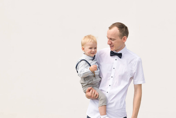 Concept père et fils. Père porte l'enfant dans ses mains en fond de mur blanc avec espace de copie - Photo, image