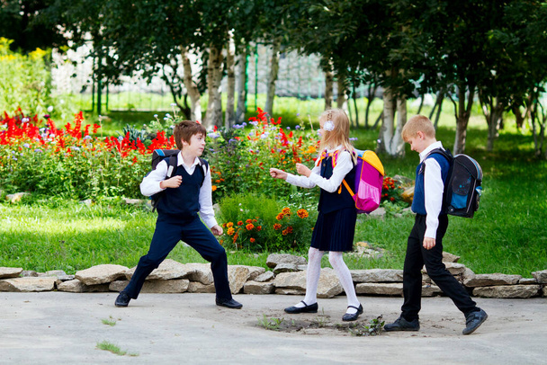 Back to school: three school children (boys and a girl) wearing uniform playing and laughing on the school yard - Foto, afbeelding