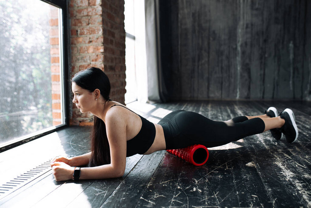 The Pilates trainer stands in a plank and works the front of the thigh with a massage roll - Fotó, kép