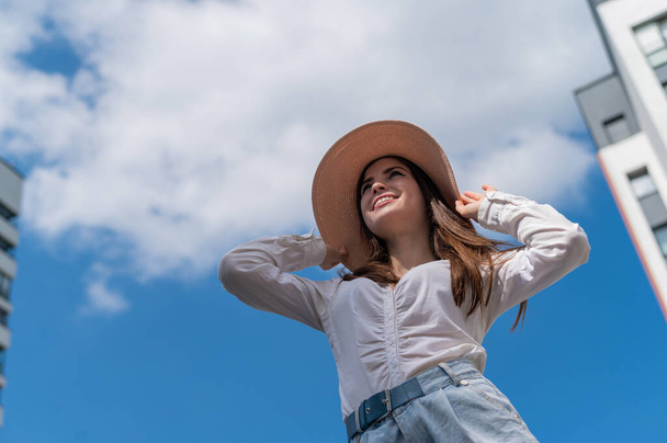 Portrait of a beautiful caucasian woman outdoors against a blue sky background. A girl wearing a hat and walking shorts on a hot summer day. - Foto, imagen
